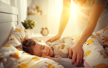 mother wakes up sleeping child daughter girl in morning.