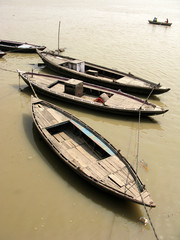 Drewniane łódki unoszące się na wodzie. Brązowa woda. Rzeka Ganges. W tle łódka z rybakami. Słoneczny dzień.