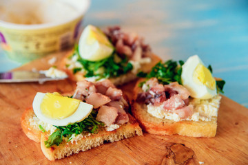 Fototapeta na wymiar bruschetta, appetizer, canapes: fish tuna and spinach on toast of white bread, with egg on wooden Board