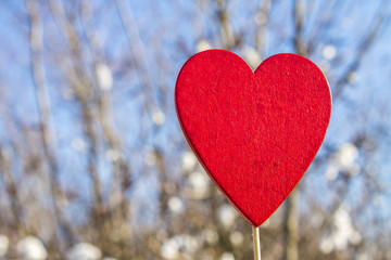 A man holds a red wooden heart on a stick against the background of nature, sky, stones. The concept of Valentine's Day.