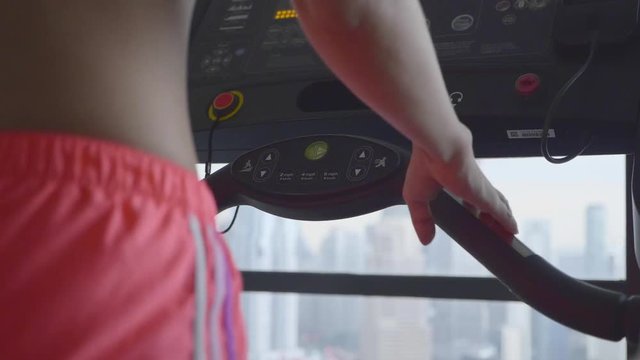 Slow motion shot of attractive young woman running on a treadmill in fitness sport club, closeup of a hand pushing buttons.Active lifestyle concept.