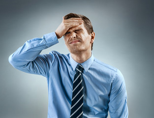 Man holding his head in pain. Photo of man in shirt and tie grimacing in pain on gray background. Medical concept
