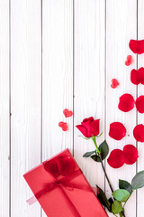 Prepare the prsesnts or surprise for Valentine's day. Red gift box near red rose and petals on white wooden background top view copy space