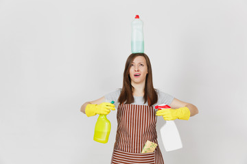 Fun housewife in yellow gloves, striped apron, cleaning rag in pocket on white background. Woman holding in hands, on head bottles with cleaner liquid for washing dishes. Copy space for advertisement.