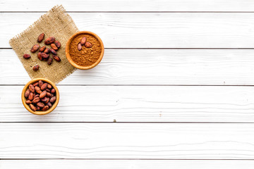 Cocoa powder in bowl and cocoa beans on white wooden background top view copy space. Popular ingregients for sweets, bakery, drinks