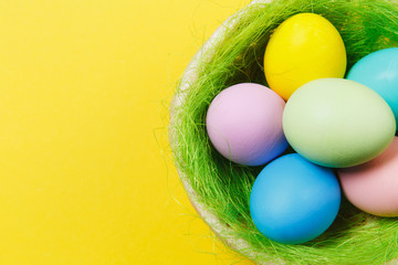 Six colorful pastel monophonic painted Easter eggs in basket with green grass isolated on yellow background. Happy Easter concept. Copy space for advertisement. With place for text. Top view on eggs.