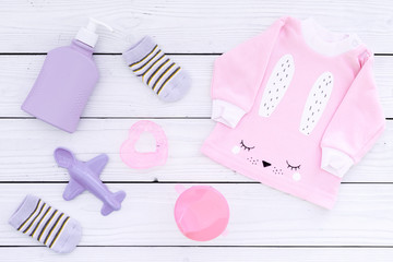 Cute pink baby clothes for girl. Shirt, booties, toy, on white wooden background top view