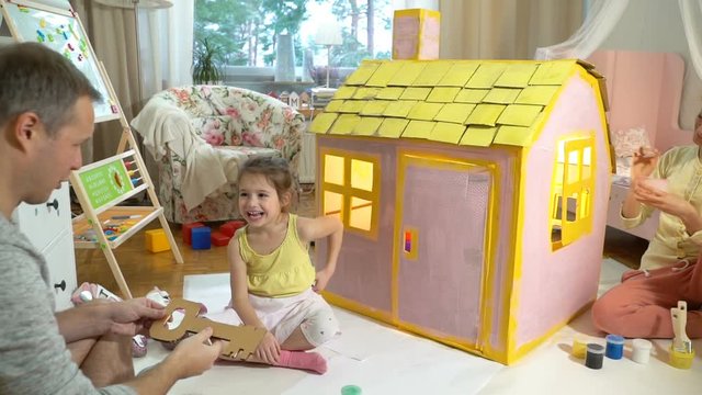 Father gives happy little girl a toy key to her new cardboard house. Slow motion-