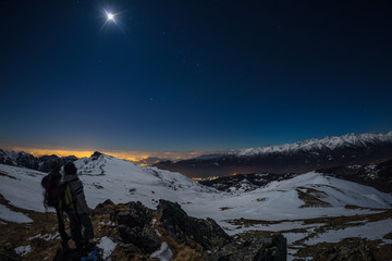 Moon and starry sky, snow on the Alps, fisheye lens. Orion Constellation, Betelgeuse and Sirio. Long exposure blurred two hikers looking at view, night outdoor activities. © fabio lamanna