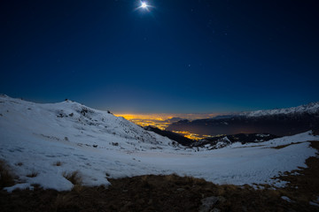 Turin city lights, night view from snow covered Alps by moonlight. Moon and Orion constellation,...