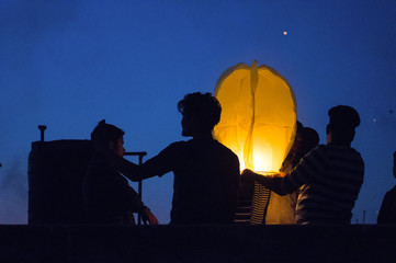 Silhouette of people standing together and flying a paper sky lantern which is lit. These lanterns have become traditional during the indian festival of makar sankranti or uttaryan in Jaipur India