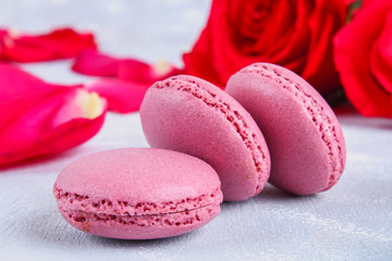 Pink and purple macaroons on a gray table surrounded by pink and white flowers.