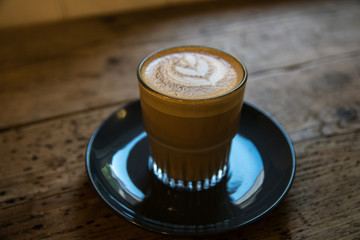 Coffee in a glass cup on a rustic table with art on top