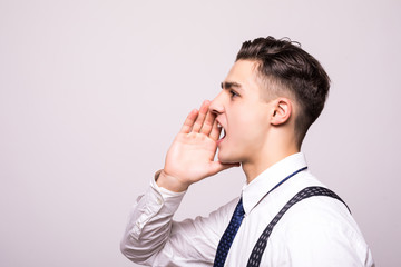 Closeup side view profile portrait, angry upset young man, worker, employee, business man, hand to mouth, open mouth yelling, isolated white background. Negative emotion facial expression emotion
