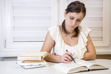 Young attractive female student with books is preparing for exams at university. Learn lessons. Education at home. Schoolgirl reading books at University of disciplines.