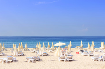 Sun beds and umbrellas on resort beach against blue sea and clear sky on bright sunny day. Beach holiday concept. Summer vacation. Tropical beach and relax.