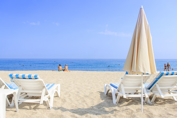 Sunbeds and umbrella on sea beach with white sand on the background of sea and blue clear sky. Summer vacation on tropical beach concept.