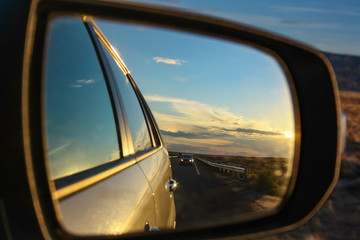 Reflection of colorful sunset. Side-view mirror during a journey. Driving at high speed on highway.
