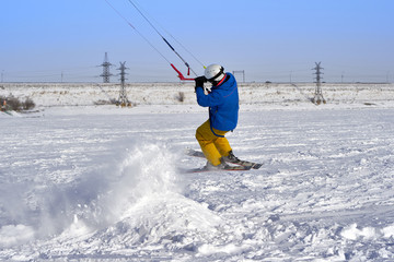 A male athlete engaged in snow kiting on the ice of a large snowy lake. He performs the jump. Winter sunny frosty day. Close-up.