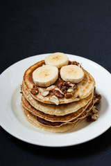 Pancakes with nuts, honey and banana in a plate on a dark background Menu , restaurant recipe concept. Served in