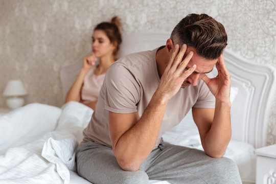 Sad man sitting on bed with his girlfriend on background