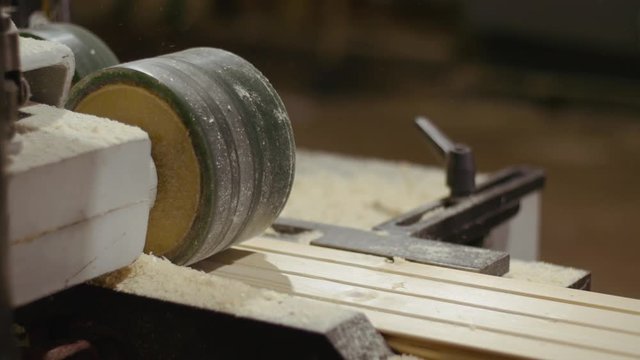 Wood board running out carpenter jointer machine at sawmill factory, lots of sawdust