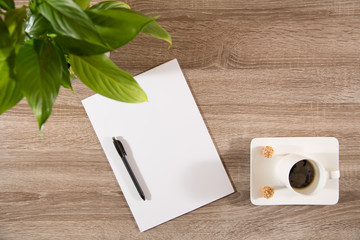 coffee on table with green plant, coffee beans and white blank paper and pen