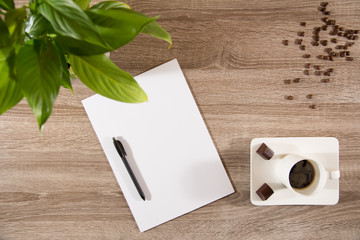 coffee on table with green plant, coffee beans and white blank paper and pen