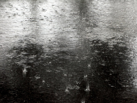 Raindrop hitting on asphalt road. Background flooded road with splash from the raindrops. Rain on pavement creating ripples.