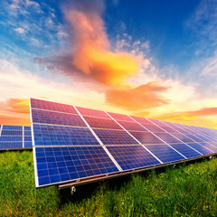 Solar panel on beautiful orange sundown background. Green grass and cloudy sky. Alternative energy...