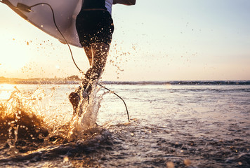 Closeup image water splashes from surfer's legs run in ocean with surfboard