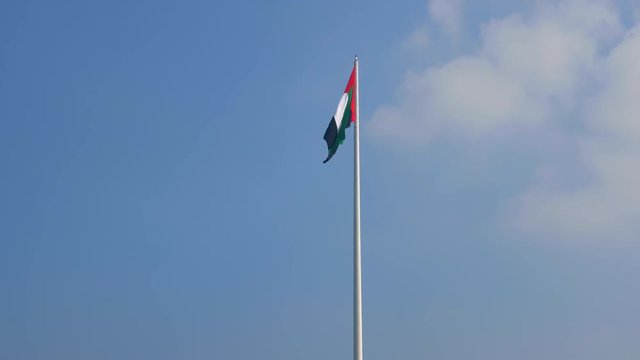 A United Arab Emirates flag flying against blue sky with clouds. UAE celebrates it