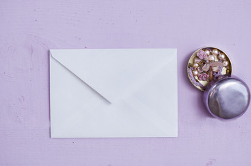 white envelope with jewelery in a round metal box flat lay on a lilac background