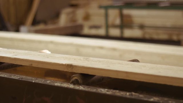 Wood plank running into carpenter jointer machine at sawmill factory, lots of sawdust