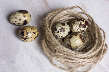 Quail eggs in a coffee cup and a bird nest with leaves on a white wooden background