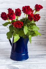 Bukiet czerwonych róż w niebieskim dzbanku na drewnianym stole - obrazy, fototapety, plakaty