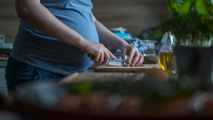 Close up pregnant woman with knife on kitchen cuts mushrooms