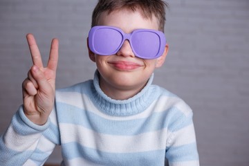 Cute smiling boy in violet sunglasses with opaque lenses showing victory gesture