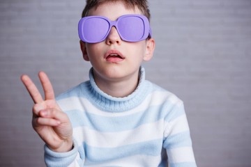 Cute boy in violet sunglasses with opaque lenses showing victory gesture
