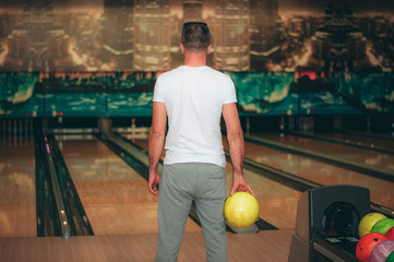 man is playing bowling. A man is standing with his back in a white T-shirt