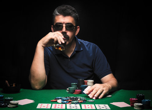 Man is playing poker. drink whiskey, man holds cards on table, winning all the chips on bank. Concept of victory