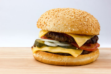 Burger close-up on a wooden table. A large burger with a beef cutlet, tomatoes, cheese, pickled cucumbers and onions on a wooden table.