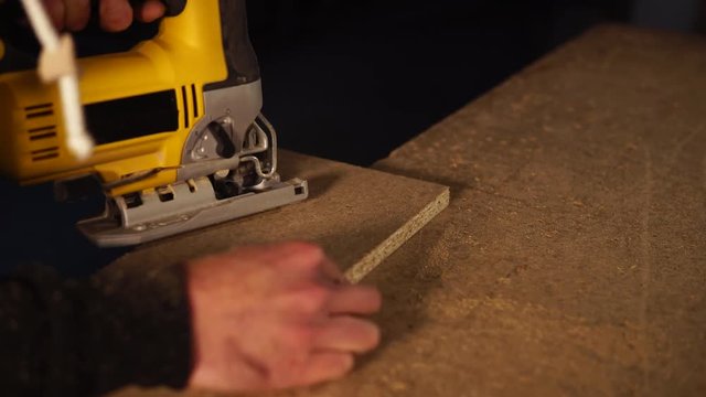close up shot of the man's hands, who cuts off a piece of chipboard, a worker uses an electric tool in order to cut off a small square from the board