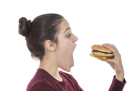Adolescent girl opening her mouth wide to eat a hamburger, on a white background.