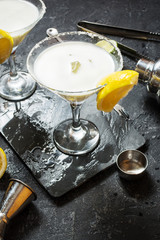 Alcohol cocktail margarita on a black stone table, with lemon. lime and shaker