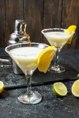 Alcohol cocktail margarita on a black stone table, with lemon. lime and shaker