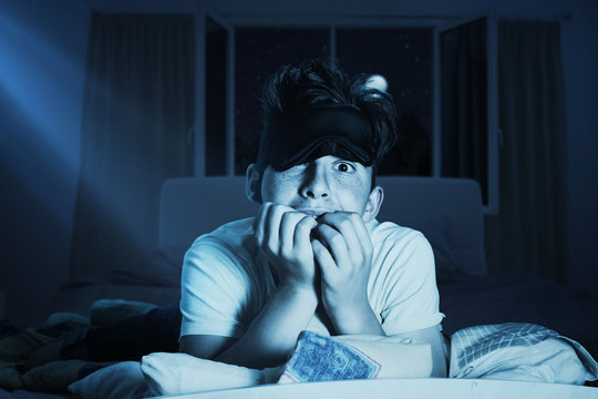 Angstvoller Junge mit Schlafbrille und zerzausten Haare kaut an den Fingernägel vor Schlaflosigkeit