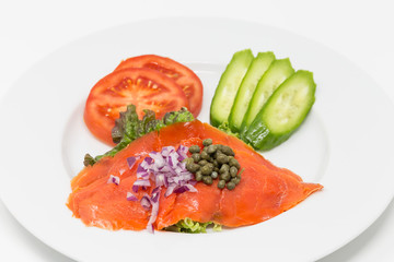 Smoked salmon salad with red onion, capers, tomato and cucumber on the white plate. 