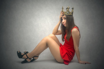 Tired and pensive woman queen is sitting on the floor and is thinking isolated on dark background.