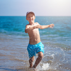 Smiling european boy is running along the sea shore.